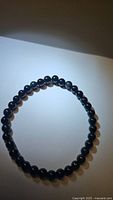 Round black beads with light rainbow flash laid flat in a circle on a white background, showing the bracelet's shape and bead size.