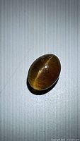 Oval-shaped cat's eye apatite gemstone showing distinct chatoyancy effect under direct lighting on a plain surface.