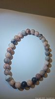 Close-up image of the natural Rodochrosite stretchy bracelet showing round polished beads in shades of pink, grey, and cream laid flat in a circular shape on a neutral background.