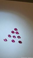 Ten untreated natural oval cut rubies shown on a pale blue background revealing color and cut.