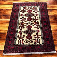 Full view of the Baluchi handmade rug showing geometric design and color scheme on wood floor background.