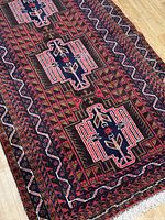 Close-up of the rug showing geometric Baluchi motifs, red and navy blue colors, and intricate border patterns.