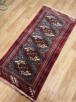 Full view of red, blue, brown geometric handmade runner rug with fringed ends on wooden floor.