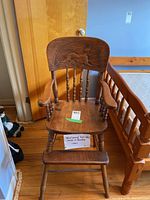 Full view of the antique wooden high chair showing seat, arms, backrest with horse carving and footrest.