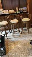 Set of three wicker bar stools positioned in front of a bar counter, showing their overall design and condition.