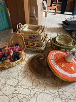 Overview photo showing stacked rectangular woven baskets with hand-painted flowers, round baskets, and flower-shaped woven napkin rings.
