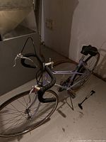 Side angled view of the blue road bike revealing frame, handlebars, wheels and pedals. Portable pump visible on floor to the right.