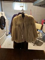 Front view shows the hanging fur coats on hanger with one coat more visible in light beige/cream tone fur.