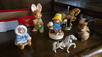 Six vintage animal figurines displayed on a shelf, including a rabbit, bear, horse, Eskimo child, brown cat, and rocking horse.