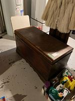 Full view of vintage wooden storage chest with hinged lid, dark brown finish, placed on basement floor.