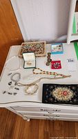 Full overview of clutches, necklaces, charms, earrings, and brooches laid on dresser