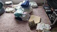 Wide shot of the assorted linens arranged on carpeted floor with labels and tags visible on some stacks