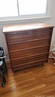 Full view of the Mid-Century Modern style wooden dresser with five drawers, showing general condition and size relative to surroundings.