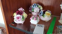 Four porcelain flower arrangements displayed on glass shelf, multicolored flowers, three Radnor and one Paragon