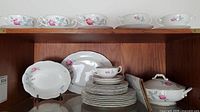 Shelf display of plates, cups, saucers, platters, and covered bowl with pink rose design