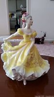 Front angle of Royal Doulton Ninette figurine highlighting the yellow dress and detailed face.