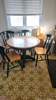 Full view of round wooden kitchen table with four chairs placed around it, showing condition and style.