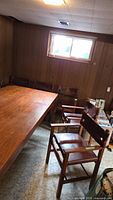 Eight teak chairs arranged around a wooden table in a paneled basement room.