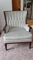 Front view of vintage wooden framed chair with beige tufted fabric upholstery.