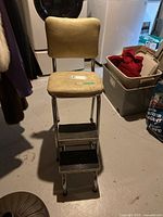 Front view of vintage step chair stool showing yellow vinyl padded seat and backrest, metal frame, two rubber steps and casters.