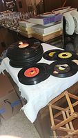 Stacked 45 RPM records and singles laid out on a white cloth with visible paper labels in various colors.