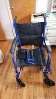 Front view of blue folding manual wheelchair with black fabric seat and backrest, armrests, large rear wheels, and front caster wheels on wood floor.
