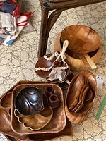 Wooden bowls and trays in various shapes and sizes including round bowls, scoops, and trays placed on a tiled floor under a wicker table.