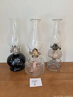 Full view of three different hurricane oil lamps side by side showing bases and chimneys.