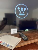 Photo showing the TV screen with the Westinghouse logo displayed, remote control on table and manual nearby.