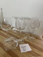 Six clear Bohemian crystal wine stem glasses arranged upright on a wooden table with a Maxsold lot card visible, showing glass clarity and stem shapes.