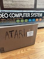 Console packaging lid reading ‘Video Computer System par Atari’ above cardboard shipping box labeled ATARI