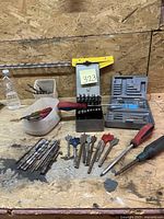Full view of collection showing various drill bits, chisel bits arranged on workbench with screwdrivers in container and drill cases.