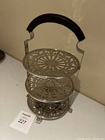 Full view of the three-tier brass cake stand showing intricate filigree pattern and black handle.