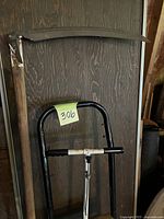 Vintage curved blade sickle and the upper portion of the wheeled dolly cart with black tubular handles.
