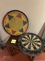 Photo showing round metal Chinese checkers board featuring colorful star design alongside a thick dartboard game.