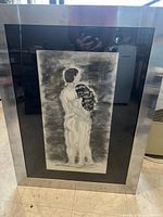 Full view of the framed black and white drawing of an embracing nude couple by Imona Natsiapik, showing the metallic frame and black matte border.