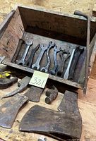 Wooden box with multiple wrench heads inside; axe and hammer heads in front of the box, showing vintage condition and rust.