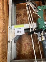 Photo showing part of aluminum extension ladder and green pole pruner with rope mechanism attached.