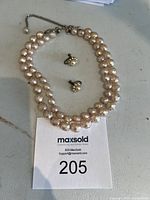 Full view of the two-string lotus pearl-like bead necklace with matching earrings lying on a surface.