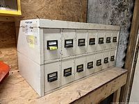 Angled side view showing metal cabinet with 14 small drawers in two rows, each drawer with handle and label holder.