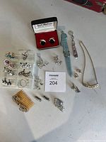 Full lot arranged on a white surface including earrings in plastic organizer, cufflinks in box, chain necklace, rings, letter opener, comb, and other small jewelry items.