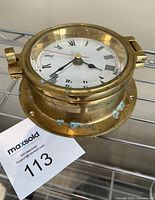 Front view of brass porthole clock showing latch, Roman numeral clock face labeled 'Victory' and some tarnish and corrosion spots on the brass exterior rim.