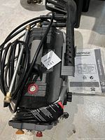 Pressure washer body with cords, hose, foam blaster attachment, and user guide booklet visible.