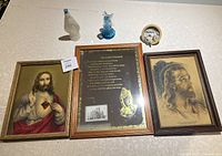 All religious items laid out on the table including framed Jesus images, Lord's Prayer mirror, glass figurines, and ceramic disc.