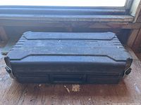 Black plastic carrying case for the rotary saw, closed and resting on a wooden surface near a window.