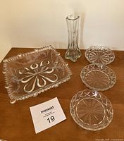 Photo showing 3 square clear glass waffle pattern coasters, a square pressed glass dish with swirl and beaded edge details, and a slender square-based clear bud vase.