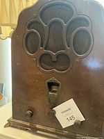 Front view of the vintage vacuum tube radio showing decorative wood speaker grill, three control knobs, and visible wear to bottom wood trim.