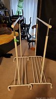 Photo of two white metal clothes racks showing horizontal bars and base rods with wheels on floor.