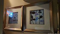 Two framed abstract flower pictures with silver frames and cream mats, showing different flower designs in blue, purple, and black