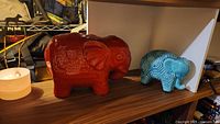 Wide shot showing both porcelain elephants on shelf, red elephant larger and turquoise smaller